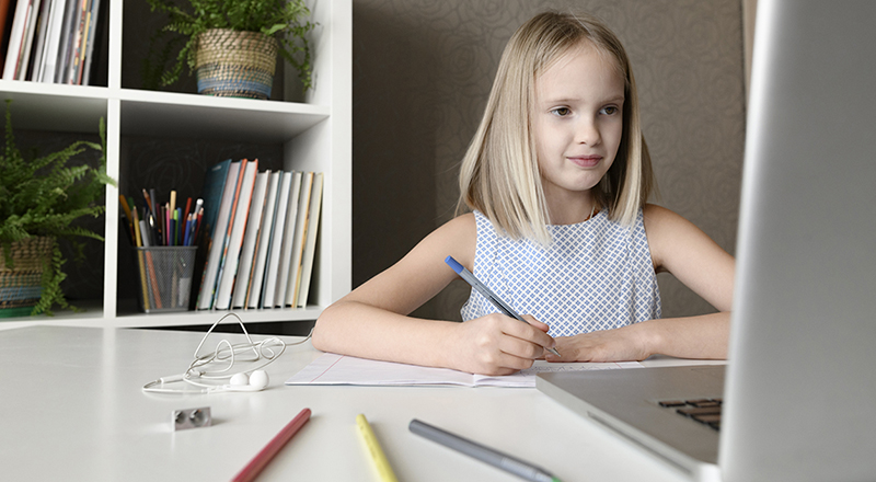 Girl sitting at table at home doing homework and using laptop